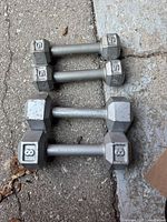Top view of four hex dumbbells laid on concrete, two smaller 5 lb pairs and two larger 8 lb pairs showing the weight embossed on ends.