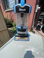 Front view of blue Shark upright vacuum cleaner showing transparent dust canister and Lift-Away label.