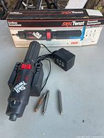 Skil Twist cordless rechargeable screwdriver with charger docking stand, charger, and three screwdriver bits displayed next to original box.