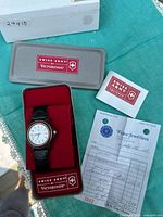 Overall lot contents including wristwatch in original Victorinox branded tin case, instruction manual, and jeweller's receipt from Fidea Jewellers.