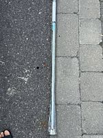 Full length view of the chrome shower rod laid out on pavement showing metallic finish and extendable ends.