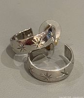 Close-up of two 14K gold hoop earrings with engraved stars and stud posts with clear plastic disc backs.