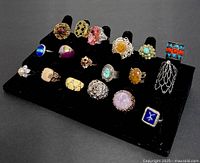Overview of 20 vintage custom rings on black display stand, showing variety of stone colors and designs