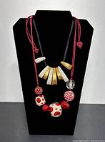 Front view of two colorful Mid-Century Modern lucite necklaces on black mannequin bust, one with gold and white curved segments and one with red and white patterned beads.