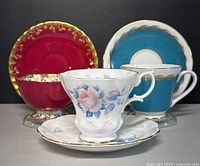 Three vintage English porcelain teacups and saucers front view showing different colors and decorative gold accents.