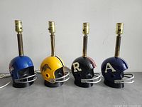Front view of four CFL helmet table lamps unlit, showing team decals and lamp rods