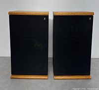 Front view of the pair of Acoustic Research speakers with black grille covers and wood trim on top and bottom.