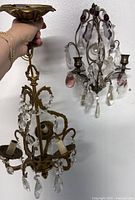Hand holding antique brass ceiling chandelier, showing detailed view of crystal prisms and candle holders.