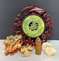 Photo of seven pieces including circular faux jade wall decor with dark red resin carved frame, three carved mythical animal figurines, cylindrical carved piece, and two flat carvings.