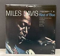 Front cover photo of the Miles Davis Kind of Blue vinyl album showing Miles Davis playing trumpet with dark background and colored text.