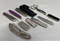 Full view of all eight vintage collectible pocket tools spread on white surface showing different types including corkscrews, lighter, scissors multi-tool, nail files and small case.
