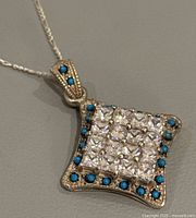 Front view of the vintage sterling silver pendant showcasing clear center stones and turquoise-blue border stones.
