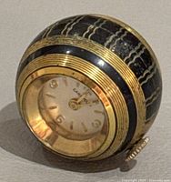 Image of vintage Caravelle watch pendant showing the round dial and gold-tone patterned casing with black textured design.