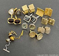 Top-down view of entire cufflinks collection showing all 12 pairs laid out against a black background.