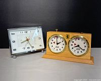 Photo showing the vintage German mechanical APFV Rolland chess clock next to a smaller chrome-framed tabletop clock.