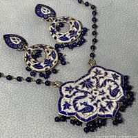 Close-up of enamel necklace pendant and earrings showing detailed floral and bird enamel design with blue bead accents