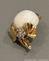 Front side close-up of the elephant brooch showing white spherical body, gold-tone ears and trunk with rhinestones on the head and green rhinestone eyes.