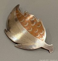 Front view of vintage leaf-shaped mixed metal brooch featuring silver and copper tones with decorative pattern.