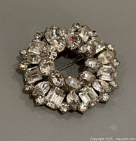 Front view of circular Weiss brooch with clear rhinestones in various shapes and sizes set in silver-tone metal.