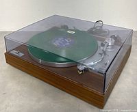 Three-quarter front view with clear dust cover closed and green test record on platter