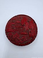 Top view of carved cinnabar round box displaying landscape relief