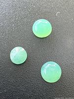 Three round green cabochon emeralds on black surface