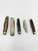 Five folding pocket knives laid out side by side