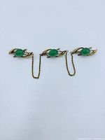 Front view of three linked gold-tone scarf clips with green stones
