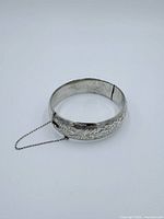 Full view of hinged sterling cuff bracelet showing engraved floral pattern and safety chain