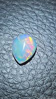 Close-up photo of a pear-shaped Ethiopian opal cabochon showing its translucent body and vibrant rainbow play of color on a black textured background.