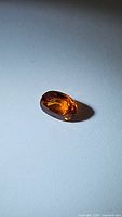 Close-up image of an oval faceted spessartite garnet with bright Fanta orange color on a white background, highlighting the gemstone's clarity and cut.