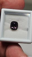 Cushion cut spinel mounted in white display case held between fingers