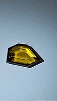 Natural fancy cut African sphene gemstone lying flat on a light surface, displaying its yellow-green color and facets.