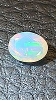 Close-up of oval cut faceted Ethiopian opal on black textured surface, showing play of colors.