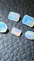 Five natural Ethiopian opals with mixed faceted cuts on a textured dark surface showing their multicolored flashes.
