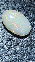 Oval cabochon cut opal resting on black textured surface showing multicolored fire with predominant warm tones