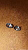 Photo showing two pear shaped, light blue natural aquamarine gemstones on a brown textured surface.