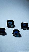 Four octagon cut blue sapphires placed on a surface lit with direct light showing their color and shape.