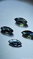 Four marquis cut natural blue sapphires arranged on a white surface showing high luster and deep blue color.