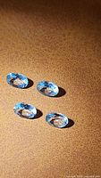 Four natural sky blue oval cut topaz gemstones on a textured brown background, showing light reflecting off the facets.