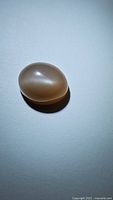 Close-up of the 6.92ct peach catseye moonstone showing its smooth oval shape and reflective catseye band.