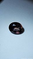 Oval cut natural sapphire gemstone with color change effect, photographed on a light blue surface under varied lighting to show color shift.