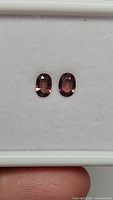 Pair of oval-shaped sapphires with a slight purple-pink-orange color on white background close-up.