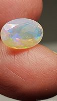 Close-up photo of a faceted oval Ethiopian opal gemstone held between fingers showing multicolored flash and translucency.