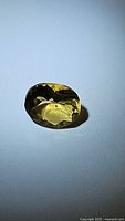 Oval cut golden citrine gemstone on a neutral background displaying facets and color.