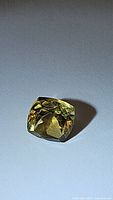 Photo of natural golden citrine gemstone cushion cut, displayed on light surface showing gemstone clarity and color