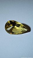 Natural golden citrine pear cut gemstone photographed on a plain background showing facets and color.
