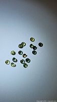 Photo of 19 small natural oval green sapphires with diamond cuts laid on white background, showing their high clarity and color.