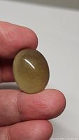 Handheld photo showing the oval lemon citrine cabochon with yellow tones and polished surface.