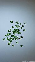 Scattered small green tsavorite garnet gemstones on white background showing variety of shapes and sizes in mixed cuts.
